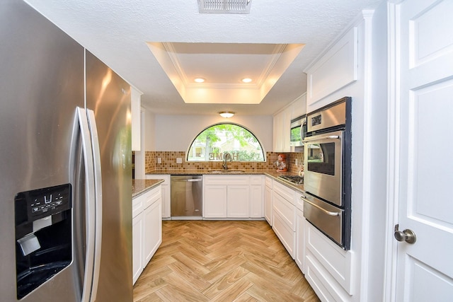 kitchen with appliances with stainless steel finishes, a sink, a warming drawer, ornamental molding, and a tray ceiling