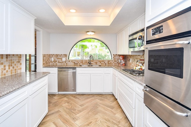 kitchen with appliances with stainless steel finishes, a sink, a tray ceiling, ornamental molding, and a warming drawer