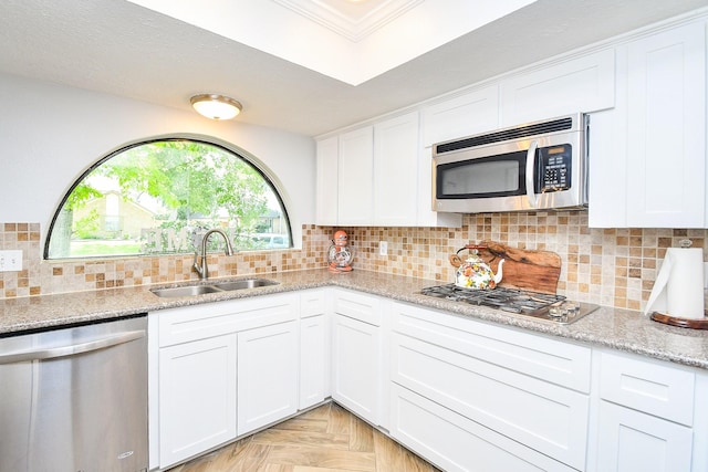 kitchen with white cabinets, light stone counters, a sink, stainless steel appliances, and decorative backsplash