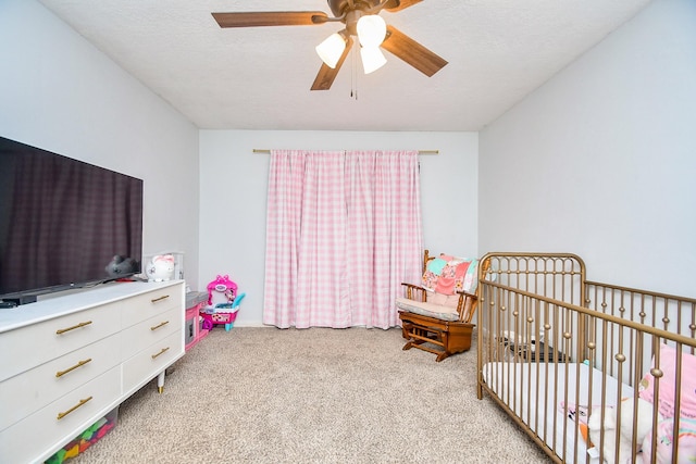 carpeted bedroom with a crib and a ceiling fan