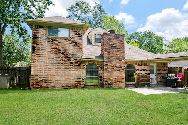 rear view of property featuring brick siding, a patio, fence, and a lawn