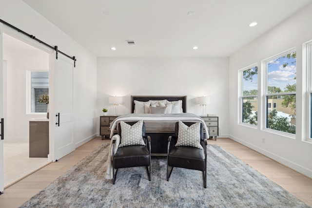 bedroom with light wood finished floors, a barn door, baseboards, visible vents, and recessed lighting