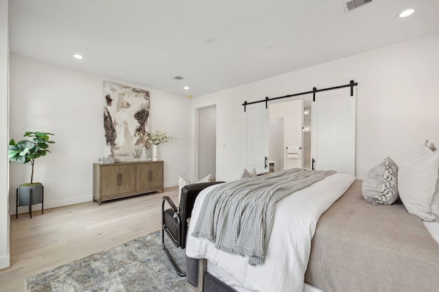 bedroom with a barn door, light wood-style floors, baseboards, visible vents, and recessed lighting