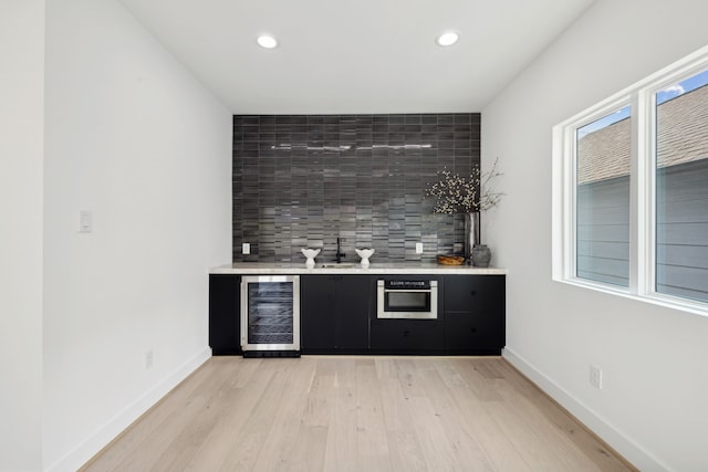 bar with backsplash, wet bar, light wood-style flooring, and wine cooler