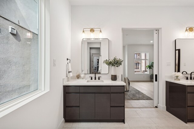 full bath featuring two vanities, tile patterned flooring, a sink, and baseboards
