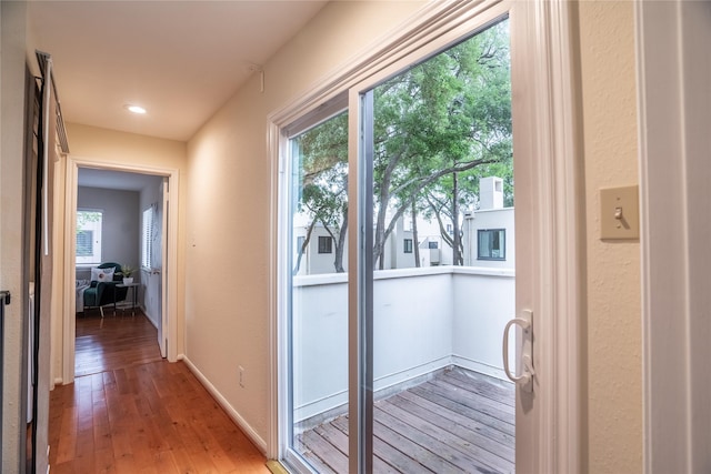 doorway featuring baseboards, a textured wall, and light wood finished floors