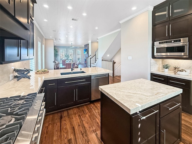 kitchen with a sink, stainless steel appliances, a peninsula, ornamental molding, and dark wood-type flooring