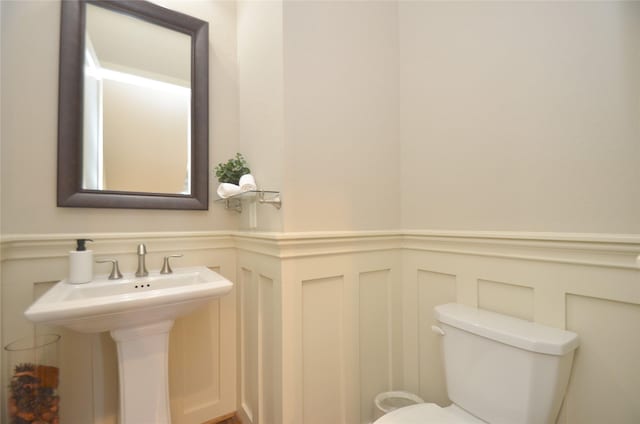 half bath with a decorative wall, toilet, a sink, and wainscoting