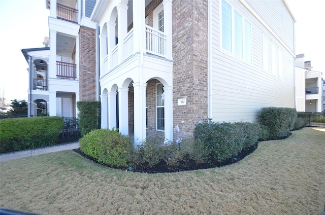 view of side of property with brick siding, a yard, and a balcony