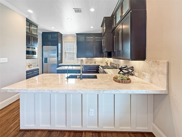kitchen with a sink, backsplash, a peninsula, appliances with stainless steel finishes, and visible vents