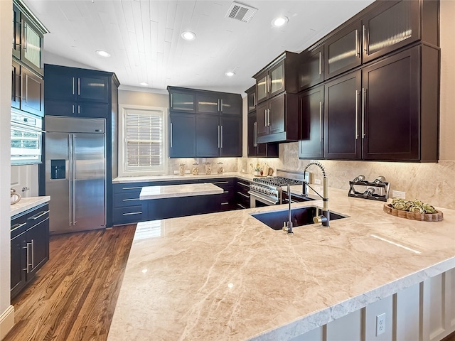 kitchen with high end appliances, glass insert cabinets, a peninsula, dark wood-style flooring, and visible vents