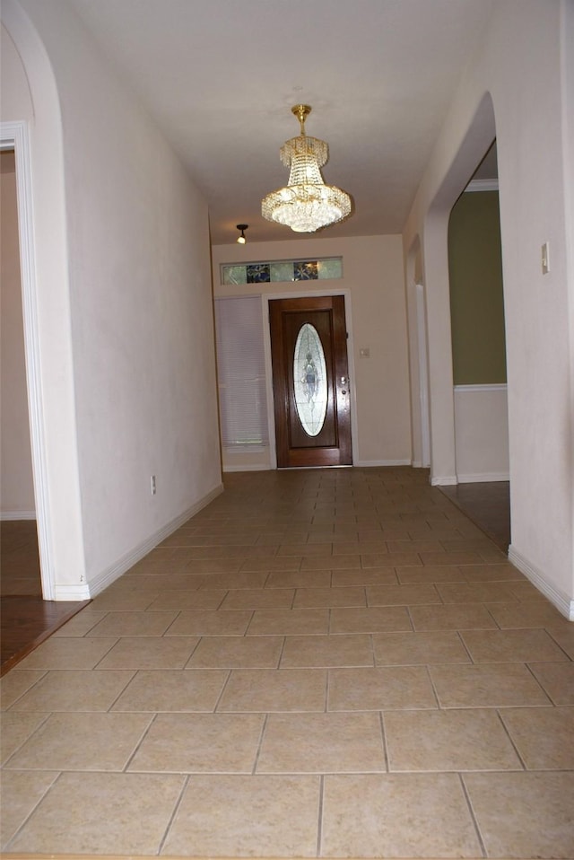 foyer featuring light tile patterned floors, arched walkways, an inviting chandelier, and baseboards