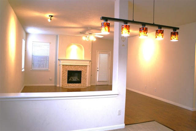 unfurnished living room featuring a tile fireplace, ceiling fan, wood finished floors, and baseboards
