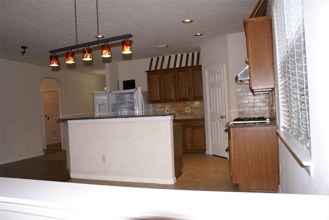 kitchen featuring recessed lighting, arched walkways, brown cabinetry, a kitchen island, and backsplash
