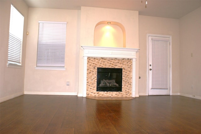 unfurnished living room with wood finished floors, a tiled fireplace, and baseboards