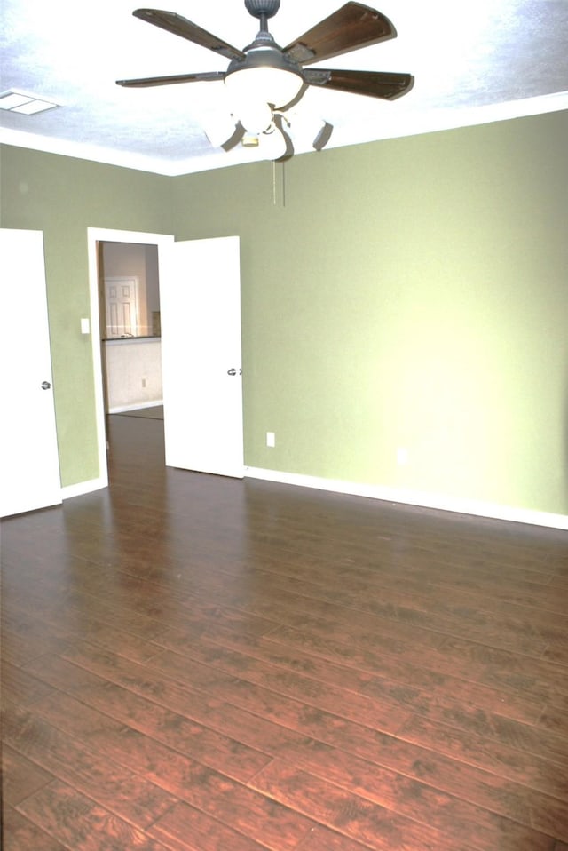 empty room featuring baseboards, visible vents, ornamental molding, and dark wood-style flooring