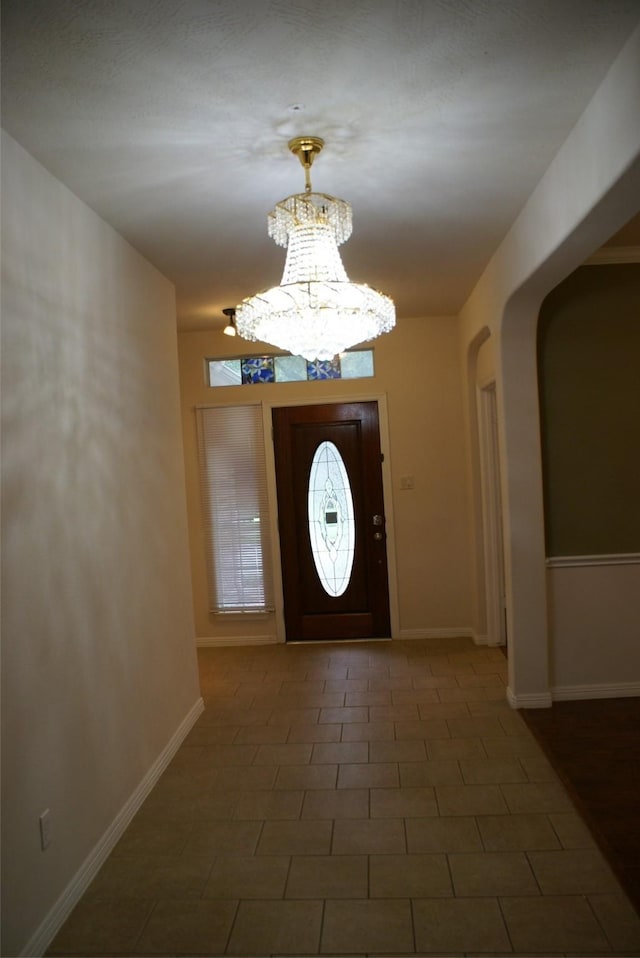 foyer entrance with arched walkways, a chandelier, and baseboards