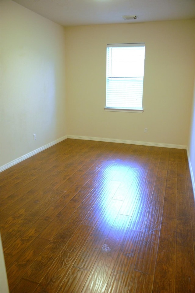 unfurnished room featuring dark wood-style flooring, visible vents, and baseboards