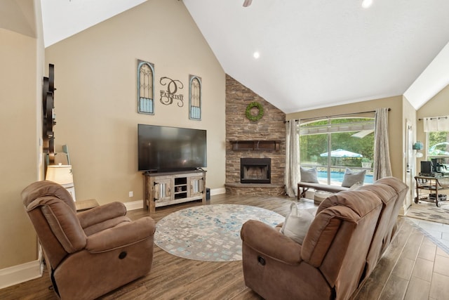 living area featuring baseboards, high vaulted ceiling, wood finished floors, and a stone fireplace