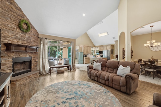 living room featuring light wood finished floors, an inviting chandelier, a fireplace, high vaulted ceiling, and arched walkways