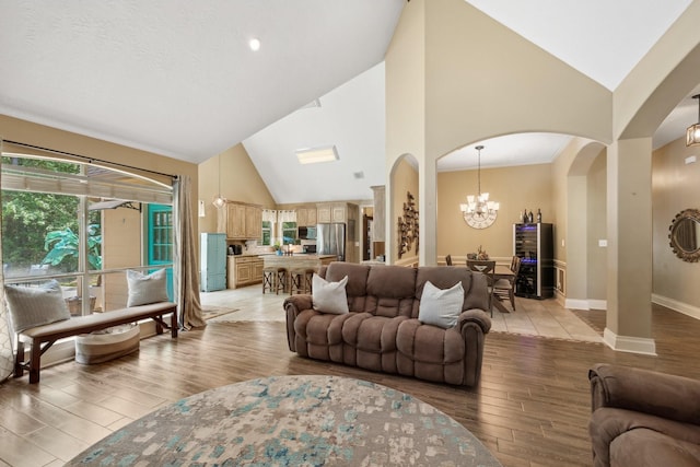 living area featuring baseboards, arched walkways, light wood finished floors, high vaulted ceiling, and a notable chandelier