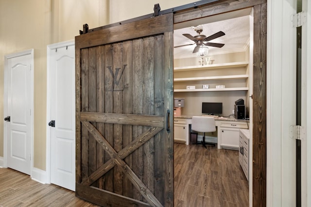 office with a barn door, a ceiling fan, dark wood-style floors, and built in desk