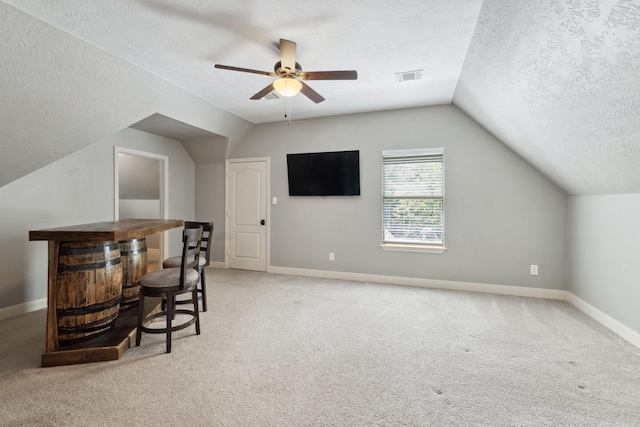 bar with visible vents, light carpet, a textured ceiling, and vaulted ceiling