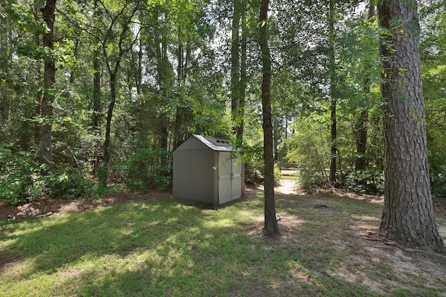 view of yard featuring a storage shed, a wooded view, and an outdoor structure