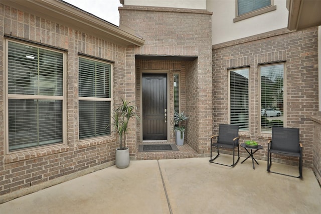 view of exterior entry with a patio, stucco siding, and brick siding