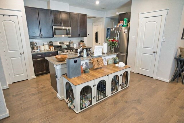 219 Lisa Marie Dr, Angleton, TX 77515 - kitchen with light wood-type flooring, appliances with stainless steel finishes, an island with sink, and dark brown cabinetry