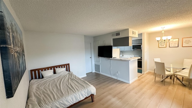 bedroom featuring light wood finished floors, visible vents, an inviting chandelier, and a textured ceiling