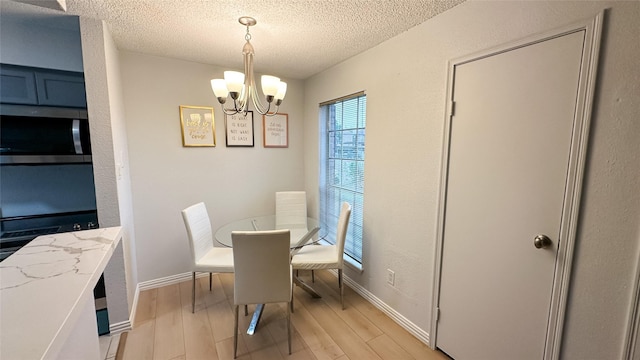 dining room featuring baseboards, an inviting chandelier, a textured ceiling, and light wood-style flooring