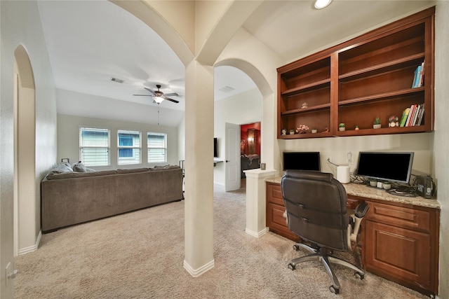 office featuring light colored carpet, built in study area, a ceiling fan, arched walkways, and baseboards