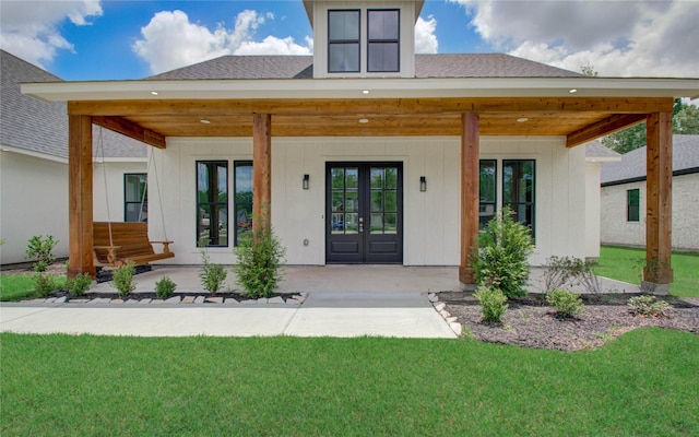 rear view of house featuring board and batten siding, french doors, roof with shingles, and a lawn
