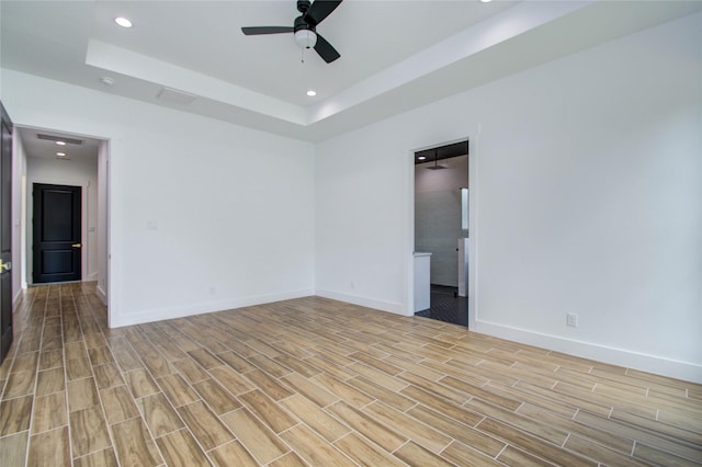empty room featuring a raised ceiling, ceiling fan, baseboards, and light wood-type flooring
