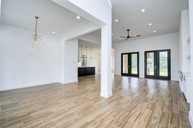 unfurnished living room with ceiling fan with notable chandelier, light wood-style flooring, baseboards, and recessed lighting