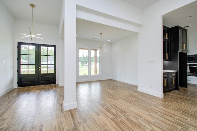 entryway featuring baseboards, light wood-style flooring, french doors, and a notable chandelier