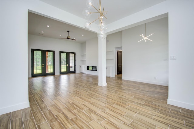 unfurnished living room featuring ceiling fan with notable chandelier, light wood-type flooring, a towering ceiling, baseboards, and recessed lighting