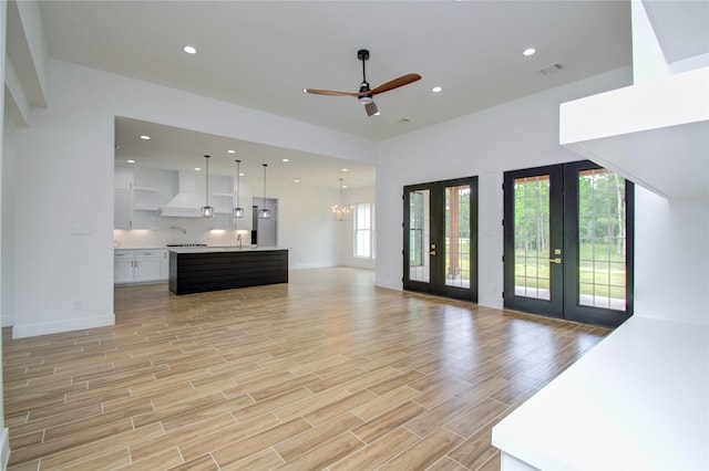 unfurnished living room with french doors, light wood-style flooring, a sink, visible vents, and ceiling fan with notable chandelier