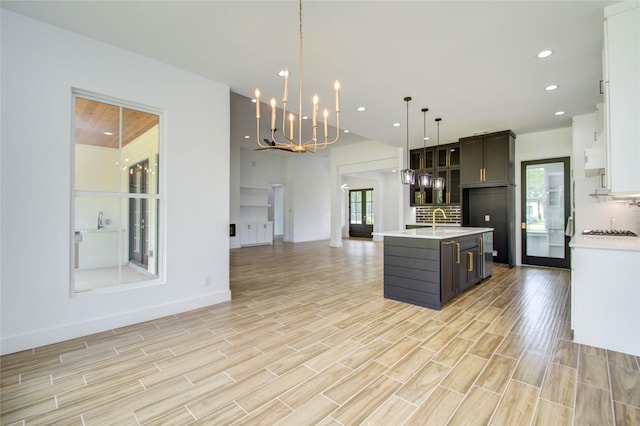 kitchen with light countertops, a sink, a chandelier, light wood-style flooring, and open floor plan