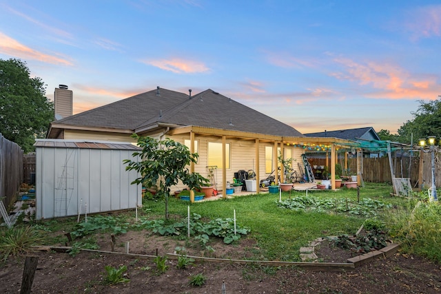 back of property at dusk with a storage unit, a garden, fence private yard, an outdoor structure, and a yard
