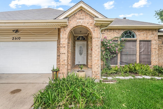 view of exterior entry featuring brick siding, roof with shingles, driveway, and a garage