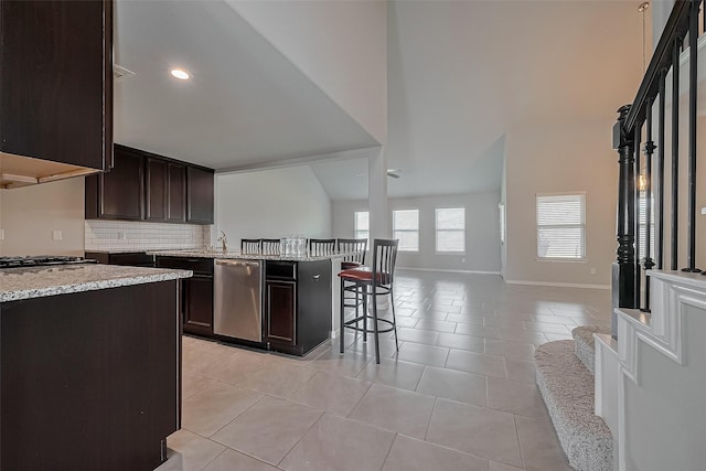 kitchen featuring light stone counters, open floor plan, dark brown cabinetry, stainless steel appliances, and baseboards