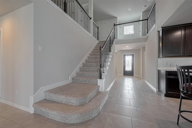 entrance foyer featuring a towering ceiling, baseboards, stairs, and light tile patterned flooring