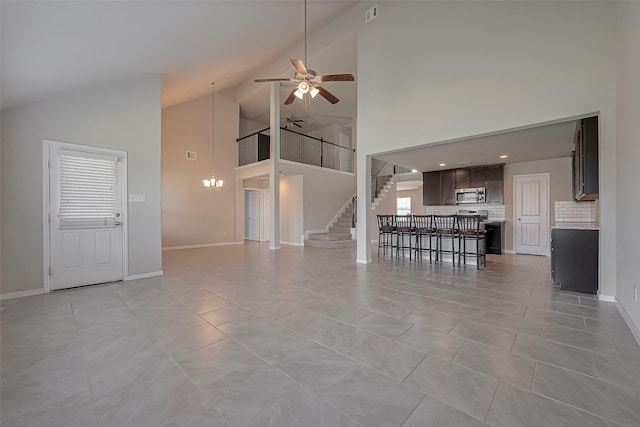 unfurnished living room with stairway, light tile patterned floors, baseboards, high vaulted ceiling, and ceiling fan with notable chandelier