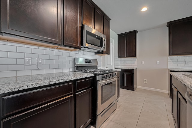 kitchen with stainless steel appliances, dark brown cabinets, decorative backsplash, light stone counters, and light tile patterned floors