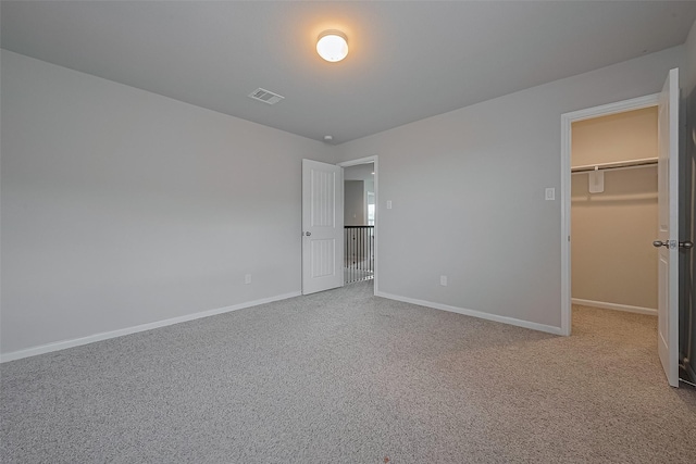 unfurnished bedroom featuring a spacious closet, visible vents, carpet flooring, and baseboards