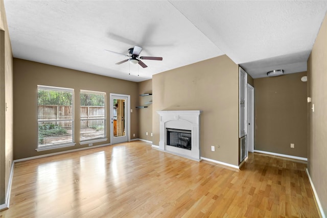 150 N Magnolia Pond Pl, The Woodlands, TX 77381 - unfurnished living room featuring ceiling fan, light wood-style floors, a fireplace, baseboards, and a textured ceiling
