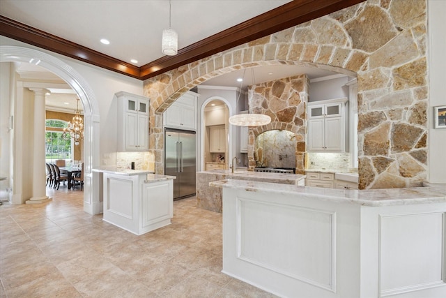 kitchen featuring an inviting chandelier, ornamental molding, decorative backsplash, built in refrigerator, and arched walkways