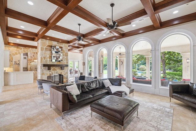 living room with beam ceiling, a ceiling fan, coffered ceiling, and a stone fireplace